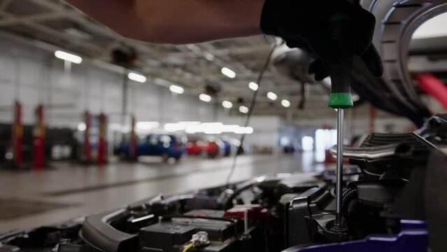 An auto mechanic unscrews the lid under the hood of the car with a screwdriver during repair at a service station
