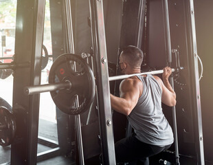 A fit asian man doing barbell back squatson the smith machine during a hot and humid day at the gym.