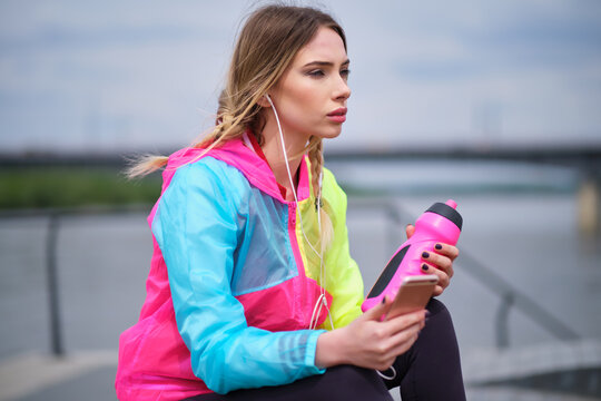 Fitness runner on mobile smart phone app tracking progress listening to music with earphones for fitness motivation. runner in sportswear relaxing sitting getting inspired.