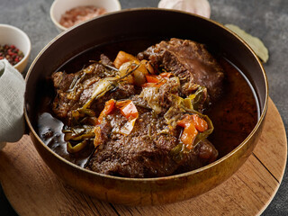 Traditional German braised beef cheeks in brown red wine sauce with herbs as closeup in skillet. - obrazy, fototapety, plakaty