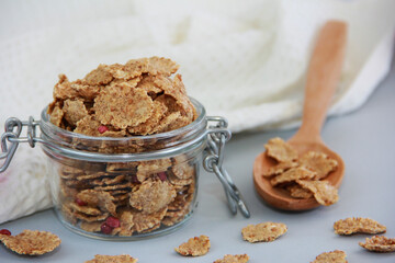 dry wheat diet muesli in a transparent glass jar with a spoon on a white background