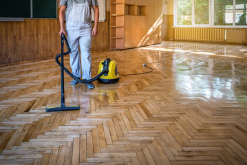 Worker cleans the parquet floor with professional vacuum cleaner