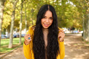 Young latin girl dressed in yellow raincoat posing looking at camera at street in autumn.