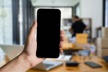 Hand holding blank smartphone with blank screen in office.