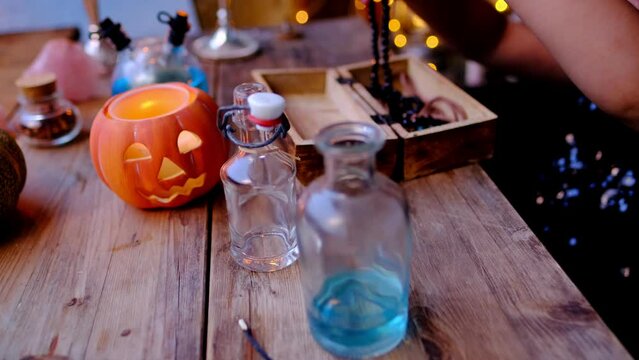 child takes out magic amulet from wooden box out of focus, girl 3 years old in witch costume and hat learns skill of magic on Halloween holiday, pumpkin jack with candle, magical attributes on table