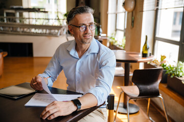 European grey man working with papers while sitting at desk in office