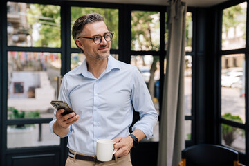 European grey man drinking coffee and using cellphone outdoors