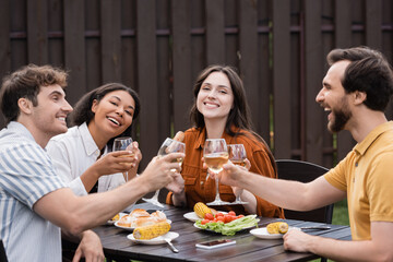cheerful multiethnic friends clinking glasses with wine and having lunch during bbq party
