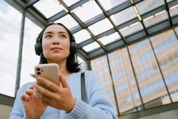 Young woman wearing headphones and using mobile phone at subway station