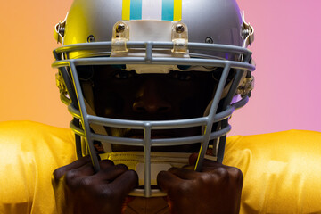 African american male american football player wearing helmet with neon yellow and purple lighting
