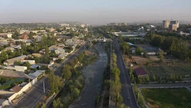 Aerial view of the city of Osh, Kyrgyzstan. Panorama of an Asian city at sunset. View of roads, cars, roofs of houses, a dried-up river, trees.