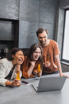 Happy Multiethnic Friends Holding Bottles Of Beer And Watching Comedy Movie On Laptop