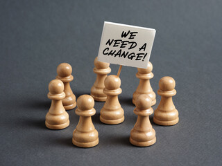 Chess pawn protester holding a sign banner with the message WE NEED A CHANGE surrounded by the...