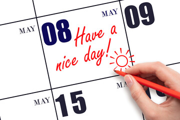 The hand writing the text Have a nice day and drawing the sun on the calendar date May 8