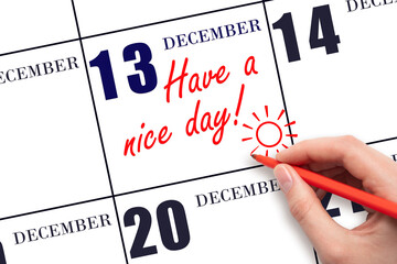The hand writing the text Have a nice day and drawing the sun on the calendar date December 13