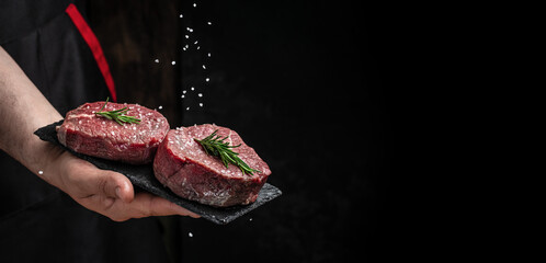 Preparing fresh beef or pork on a dark background. Chef salts steak in a freeze motion with...