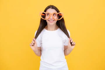 Woman feeling cool and awesome. Excited happy funny young woman in party glasses in the shape of a heart on a yellow bright background.