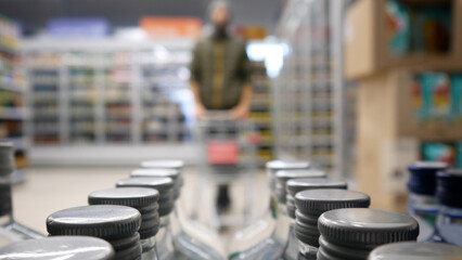 Obraz premium Close-up of many bottles of vodka or gin on a supermarket shelf and a man with a shopping trolley coming
