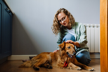 Young beautiful curly woman in glasses petting her dog