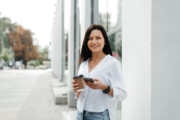 Street portrait of a young woman with a phone in her hand and a coffee to go