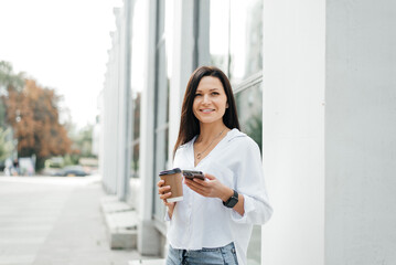 Obraz premium Street portrait of a young woman with a phone in her hand and a coffee to go