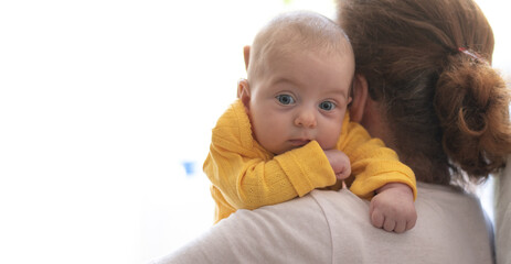Newborn with blue eyes and in yellow t-shirt lies on shoulder by grandma.  New worries in family and  lifestyle. Concept of child care, feeling safe, parent love.