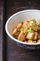 Fried tofu with sesame seeds, green onion and spices on the wooden vintage background. Homemade healthy vegetarian Asia and Japanese dish - fried tofu, close up