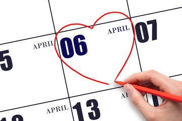 A woman's hand drawing a red heart shape on the calendar date of 6 April. Heart as a symbol of love.