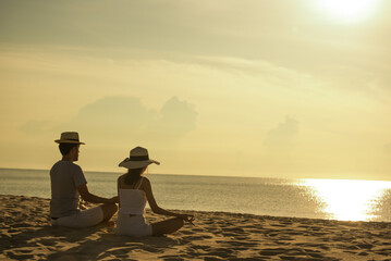 Young asian couple doing yoga exercises on the beach. lifestyle concept