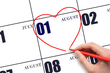 A woman's hand drawing a red heart shape on the calendar date of 1 August. Heart as a symbol of...