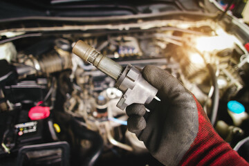A mechanic hand holds an ignition coil for a spark plug in an automobile engine,  isolated object on blurred background