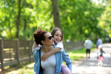 Fototapeta premium Cute young daughter on a piggy back ride with her mother.Happy family having fun outdoor