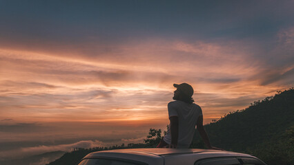 Person sitting and chilling on a Car Roof looking at the Beautiful Orange Sky during Dusk - Freedom...