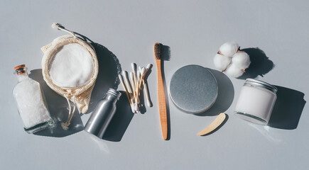 Zero waste concept. Metallic bottle and can, reusable cotton rounds. Packaging for cleaning teeth without plastic. Wooden toothbrush and glass jar with toothpaste on a gray background. Bathroom