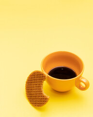 Perfect minimal breakfast concept with black coffee in the cup and sweet waffle as snack on bright yellow background. Creative layout with copy space. Aesthetic morning idea.