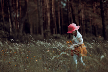  Little stylish girl in a pink hat walks in a flowering summer meadow