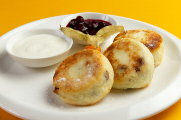 Traditional breakfast syrniki in a plate on a yellow background.