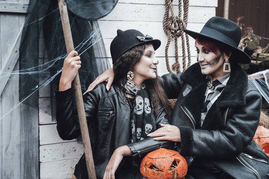 Scary family,mother,daughter celebrating halloween. Street barn. Pumpkin jack-o-lantern.Terrifying black skull half-face makeup and witch costumes, broom,stylish images hat, jackets. Children's party