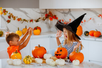 Brother and sister in halloween costumes are playing on the kitchen with decor