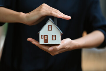 Protect your house concept. Small model of house covered by hands.