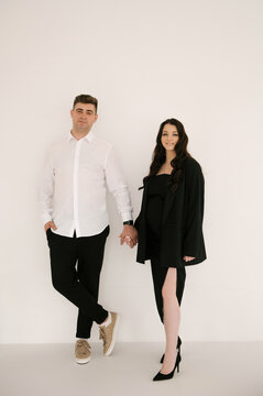 Young pregnant woman with her husband in stylish elegant black clothes on a light background