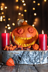 Smiling pumpkin, rowan berries and red candles on dark wooden table. Close-up