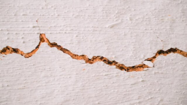 Long crack in the white ceiling of an old rural house close-up. The camera moves along a crack in the clay wall. The rapid destruction of the dwelling and the loss of integrity. after the earthquake