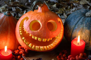 Smiling pumpkin, dry leaves, rowan berries and red candles. Close-up