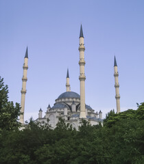 Fototapeta na wymiar Religious building a mosque made of white mineral stone with four minarets, a place of worship, in a park on a summer day