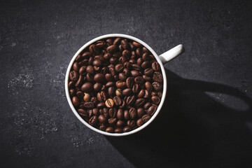 White cup of freshly brewed roasted coffee beans on gray background