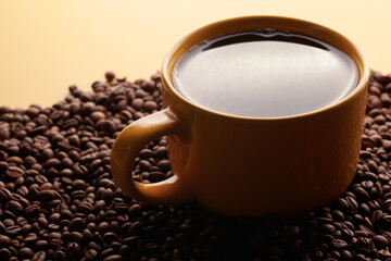 Cup of freshly brewed roasted coffee beans on yellow background