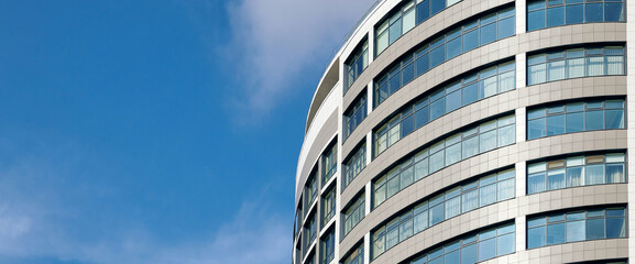 Office skyscraper high business building on blue sky background, looking up tall glass windows and steel high rise modern building. Multistory glass building with cloudy blue sky background