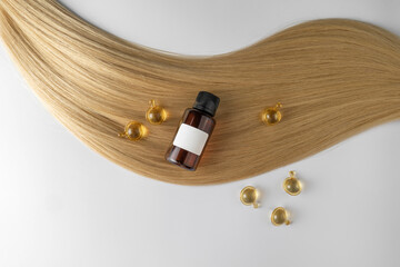 A hair care oil or serum in golden capsules lying on a strand of blond hair, product marketing mockup. A concept of hair care in a salon or at home