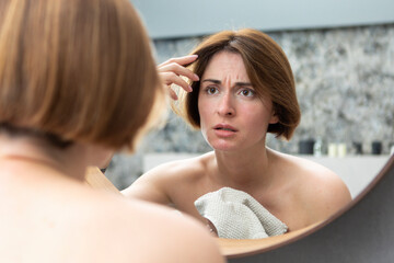 Young beautiful woman looking at mirror and confusing because of new wrinkles